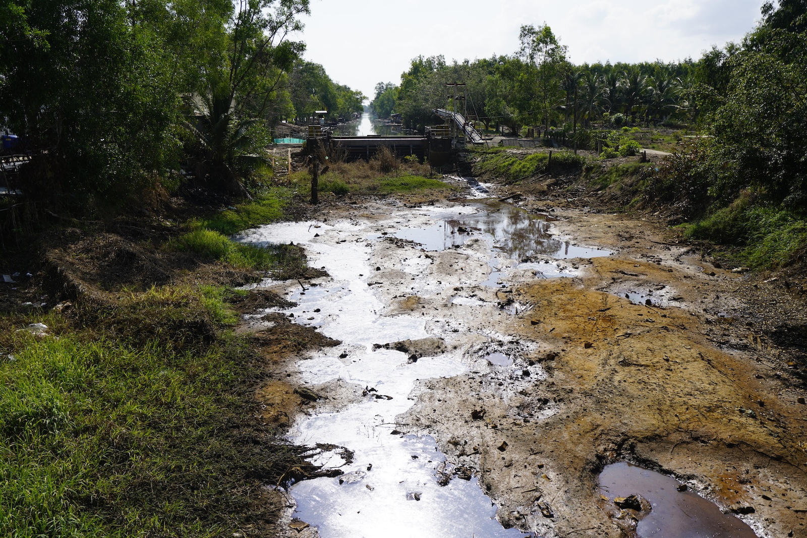 A canal drained to cracked mud below a closed sluice gate in the Mekong Delta