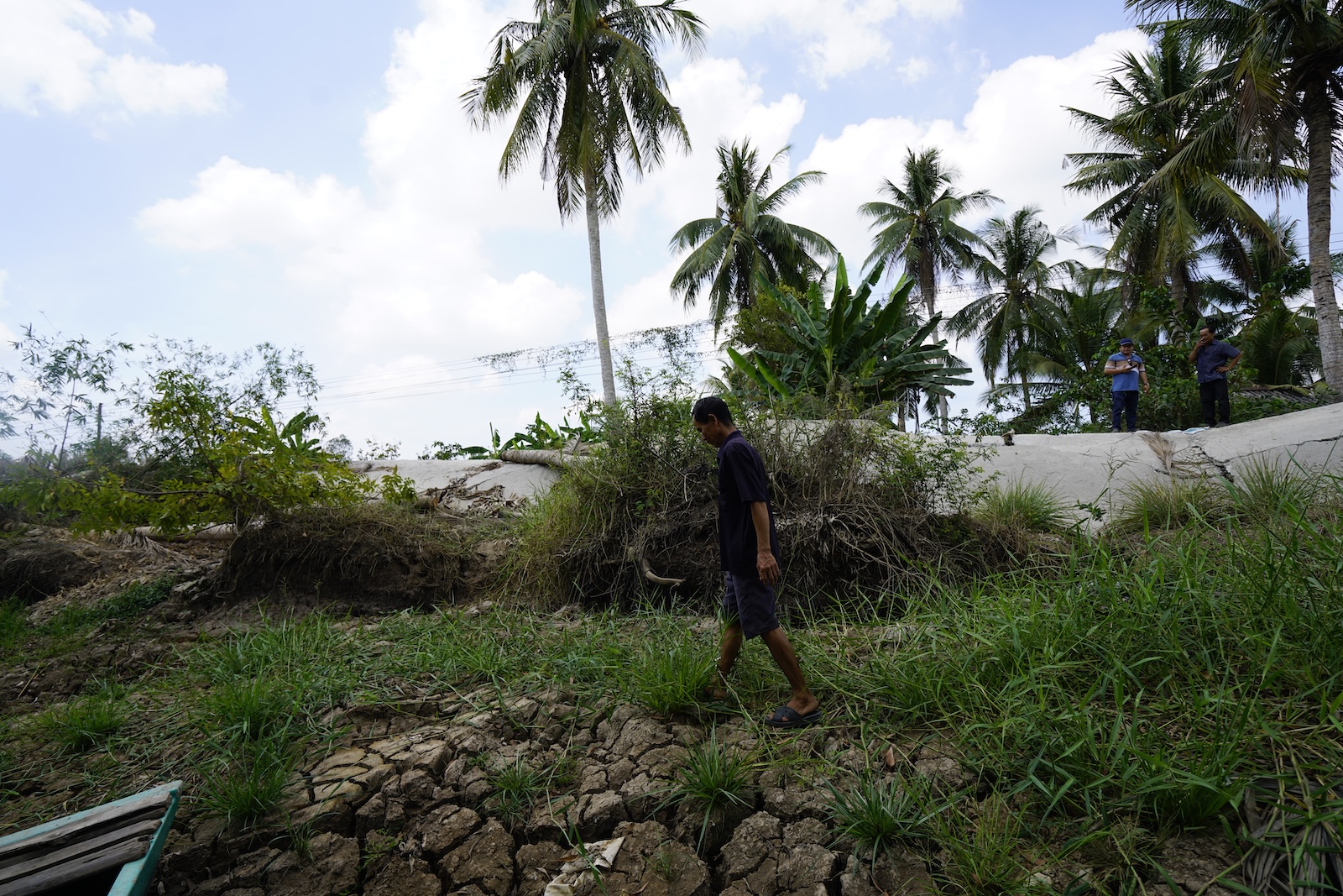 A man walks below a collapsed section of road embankment on cracked ground