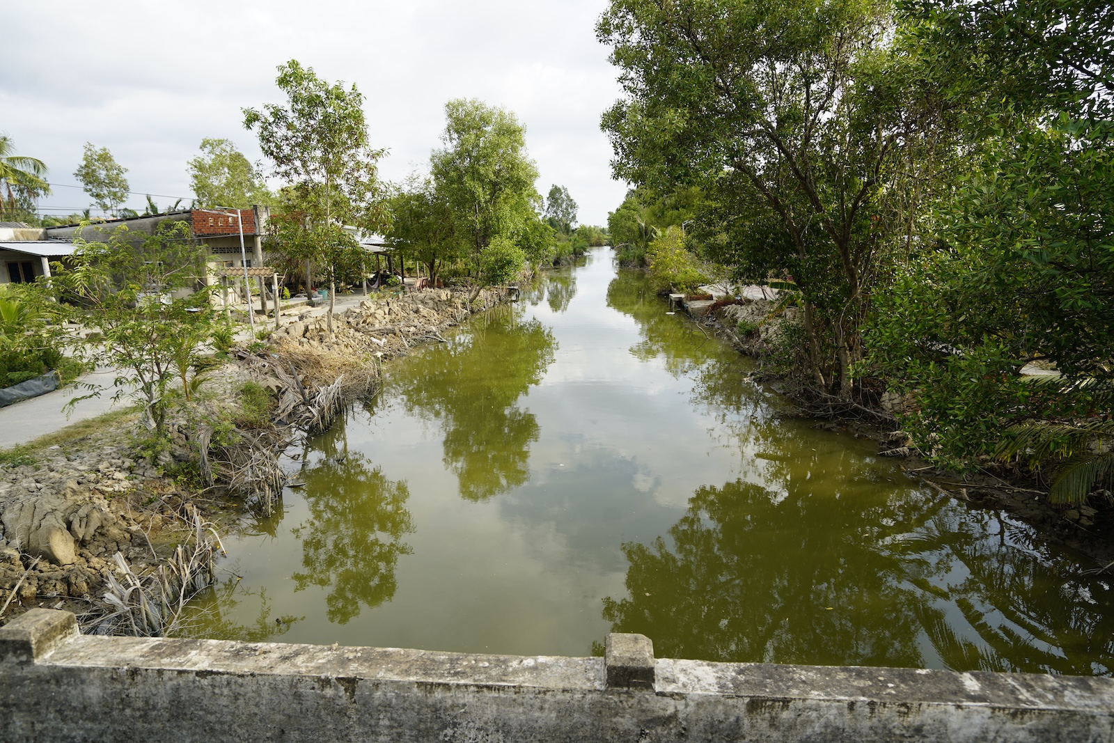 A village canal with banks armored in loose rock